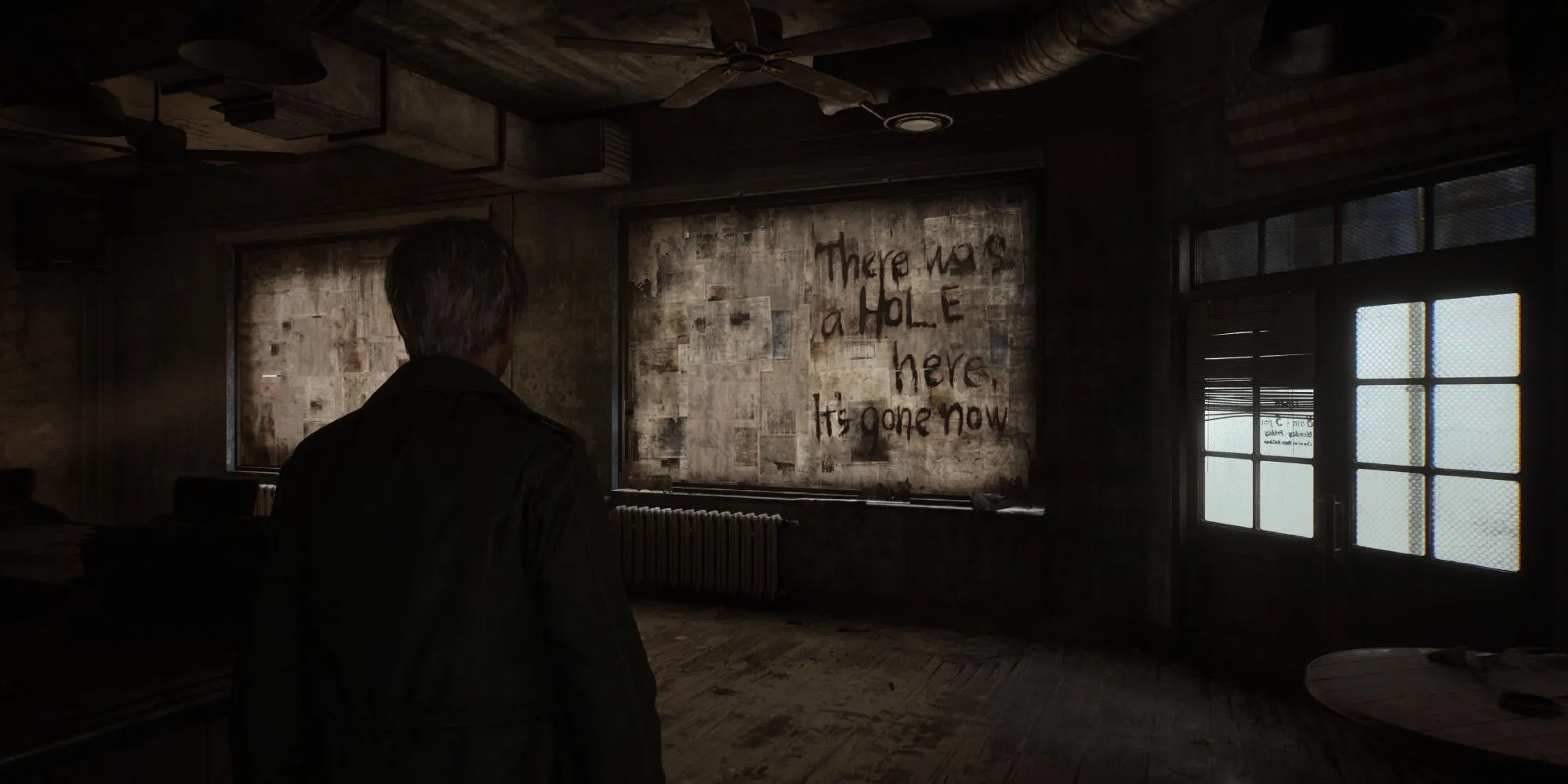Một cảnh trong Silent Hill 2 Remake với thông điệp bí ẩn trên tường và một cái lỗ dẫn xuống bóng tối